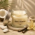 Vela aromática em pote de vidro com tampa metálica aberta, fragrância coco e baunilha, decorada com pedaços de coco, fava de baunilha e flor de baunilha ao lado