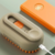 Escova a vapor elétrica 3 em 1 para gatos e cães em cor bege com detalhes laranja, conectada a cabo USB para carregamento