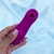 Estimulador de clitóris roxo em formato compacto segurado por mão com unhas feitas, com botão de controle visível