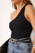 Mulher usando blusa preta feminina de um ombro só sem manga combinada com jeans azul e cinto preto