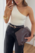 Mulher vestindo blusa feminina off white de um ombro só sem manga, combinada com calça preta e segurando bolsa marrom