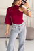 Mulher vestindo blusa vinho um ombro só com manga longa flare, combinada com calça jeans clara