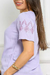 Modelo veste blusa feminina de viscose na cor Lilás com detalhes de flor nas mangas.