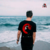Hombre de espaldas usando una playera negra con un diseño de cuervo y luna roja, frente al mar.