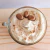 Vela capuchino en taza de café con crema suave, decorado con tres dulces en forma de grano de café y un toque de canela.