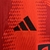 Detalhe da camisa vermelha do Bayern de Munique, mostrando o logo da Adidas em preto.