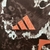 Logotipo da Adidas em bordado na camisa Bayern de Munique II 24/25, com fundo em padrões escuros e detalhes em laranja.