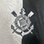 Emblema do Sport Club Corinthians Paulista, destacando âncoras e remos, em uma camisa Corinthians 3 24/25 branca e preta.