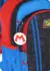 Mochila com rodinhas de Mario Bros, destacando as cores vermelha e azul e um chaveiro com o símbolo do Mario.