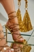 Sandália feminina de salto alto dourado com tiras brilhantes, destacando-se sobre uma superfície reflexiva.