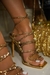 Sandália feminina de salto luxuoso com detalhes em strass dourado, destacando o pé com unhas brancas.