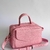Bolsa pink de couro com alça de ombro e alças manuais, apresentando um design elegante e compacto.