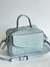 Bolsa de couro azul clara com alça e zíper, em fundo neutro.