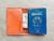 Carteira de viagem marrom com um passaporte brasileiro e uma nota de dinheiro visíveis.