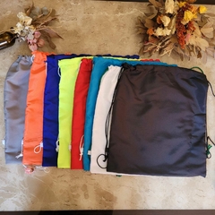 Vários sacos no formato de mochila confecionadas em tecido tactel.Diversas cores diferentes. Sacolas usadas para brindes em eventos corporativos.