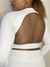 Modelo usando uma blusa manga longa branca com detalhes nas costas nuas, destacando o design moderno.