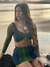 Modelo usando top e saia de tule da coleção Górgona, com estampas em azul e verde, em um cenário de praia ao pôr do sol. Roupas Femininas 