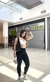 Modelo usando calça leggings negras da coleção Cianita Negra, em ambiente de shopping, com bolsa e tênis esportivos. Look Black Friday 