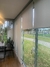 Cortina persiana rolô translúcida instalada em uma sala com vista para o exterior, mostrando a área verde e um campo de esportes.