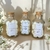 Três frascos de vidro contendo pastilhas aromáticas Wax Melts em diferentes fragrâncias: algodão, lírios e figo.