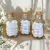 Três frascos de vidro contendo pastilhas aromáticas Wax Melts em diferentes fragrâncias: algodão, lírios e figo.