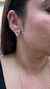 Brinco triângulo de zircônia em destaque, com acabamento dourado, na orelha de uma modelo.
