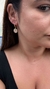 Imagem de uma mulher usando um brinco argola com pingente de olho grego cravejado de cristal, destacando a peça no ouvido. Banhado a ouro 18k. MW Semijoias