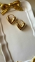 Brinco argola em forma de coração, dourado e com aro grosso, sobre um prato branco decorado com um laço dourado. Banhado a ouro 18k. MW Semijoias e Acessórios