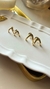 Brinco Ear Hook Dourado em exibição sobre uma base de veludo, com reflexos em um espelho ao fundo. Banhado a ouro 18k. MW Semijoias