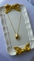 Colar Gota Liso M em semijoia com pingente dourado em forma de gota, exibido sobre uma bandeja branca decorada com laços dourados. Banhado a ouro 18k. MW Semijoias e Acessórios