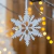 Colgante navideño en forma de copo de nieve, decorado con detalles en relieve y suspendido frente a un fondo de luces cálidas.