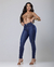 Modelo usando calça skinny jeans de tom azul escuro, com blusa top, em fundo neutro.