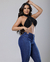 Modelo usando calça flare levanta bumbum na cor azul, com top preto, posando em fundo claro.