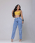 Modelo vestindo calça mom jeans azul claro e blusa amarela, posando com um sorriso.