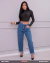 Mulher usando calça feminina jeans azul modelo Barrel da marca Tóka.21 com barra dobrada, combinada com blusa preta de manga longa justa e salto alto preto
