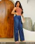 Mulher usando calça feminina wide leg jeans azul escuro com blusa regata marrom e sandálias brancas, posando em ambiente interno com porta de madeira ao fundo