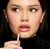 Modelo aplicando gloss labial da linha Glosslicious, com lábios brilhantes e olhar expressivo.