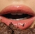 Boca com brilho gloss, destacando lábios hidratados e um pedaço de bolo de chocolate na parte inferior.