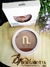 Contorno compacto Instant Matte cor Honey da Nina Make Up com embalagem branca e produto marrom em base redonda com tampa transparente, apresentado sobre superfície de madeira com flores roxas ao lado