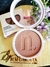 Contorno compacto Instant Matte na cor Honey da Nina Make Up com embalagem aberta e caixa ao lado, sobre superfície de madeira decorada com flores roxas