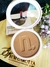 Contorno compacto Instant Matte na cor Cinnamon da Nina Make Up aberto, sobre base de madeira com flores roxas ao lado
