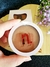 Contorno compacto Instant Matte cor Cinnamon da Nina Make Up em embalagem redonda branca sendo segurado por uma mão, com caixa e flores ao fundo