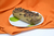 Budín marmolado de banana decorado con chispas de chocolate sobre un plato blanco, con fondo de tela naranja.