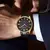 Relógio Curren masculino elegante com mostrador preto e detalhes em dourado no pulso de um homem.