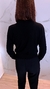 Mulher de costas usando blusa de tricô modal preta com botões de pérola na parte frontal, com cabelo castanho e ambiente interno com parede de mármore branco