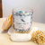 Vela aromática Cedro Real da coleção Satin Breeze, feita com cera de coco e decorada com pedras coloridas e flores secas.