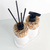 Kit lavabo Atenas com dois frascos decorativos de pedras naturais, um com bomba e outro com varetas de difusor, sobre uma base branca.