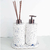 Conjunto de produtos para lavabo, incluindo um dispenser de sabão e um difusor de ambiente, ambos com acabamento em material branco com detalhes azuis.