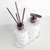 Conjunto de itens de lavabo Safira com frascos brancos decorados e tampa metálica, incluindo difusor e dispenser de sabonete.
