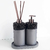 Kit lavabo Tóquio composto por dois recipientes em tons de cinza, um com dispenser e outro com varetas aromáticas, com detalhes em pedras escuras.